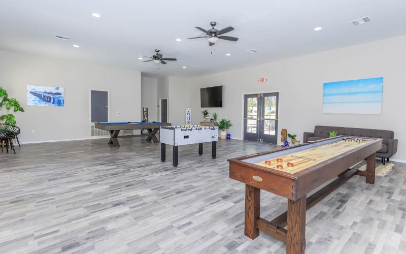 A resident clubhouse with a pool table, foosball table, a shuffleboard table, a couch, and a flatscreen television at The Solena Apartments luxury apartments in North Las Vegas, NV.